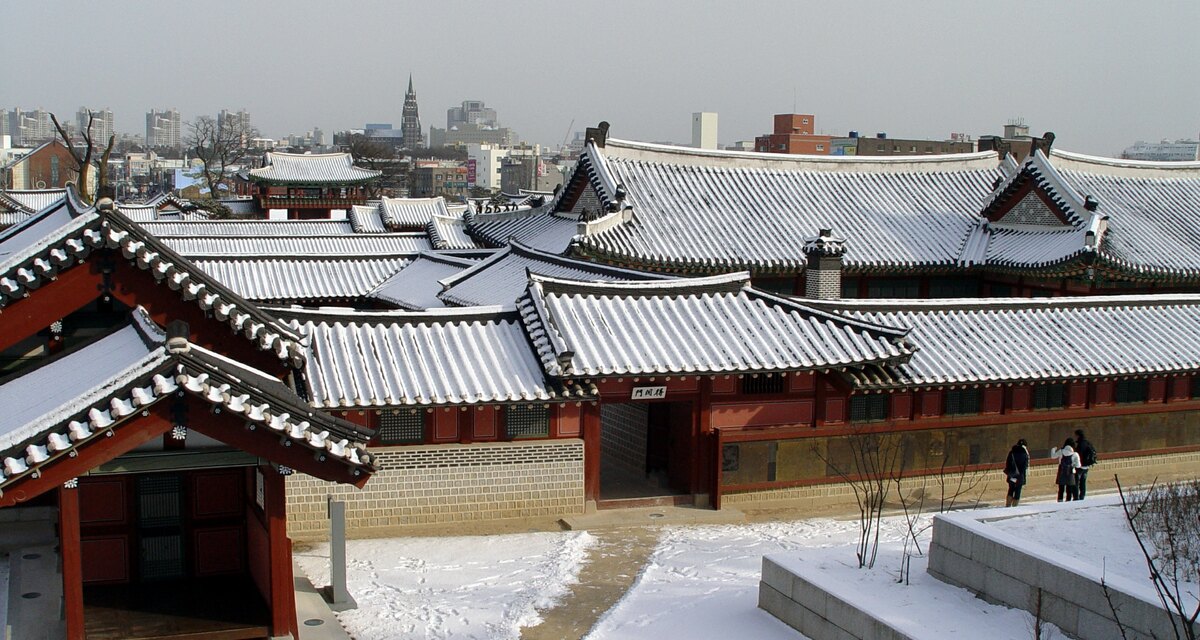 눈 덮인 수원 화성행궁의 기와지붕들과 뒤편 도심 전경